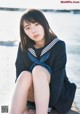 A woman in a sailor outfit sitting on a rock by the water.