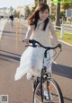 A woman in a white dress riding a bike down a street.