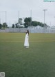 A woman in a white dress standing on a green field.