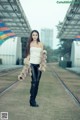 A woman in a white top and black pants standing on a train track.