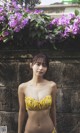 A woman in a yellow bikini standing in front of a wall.